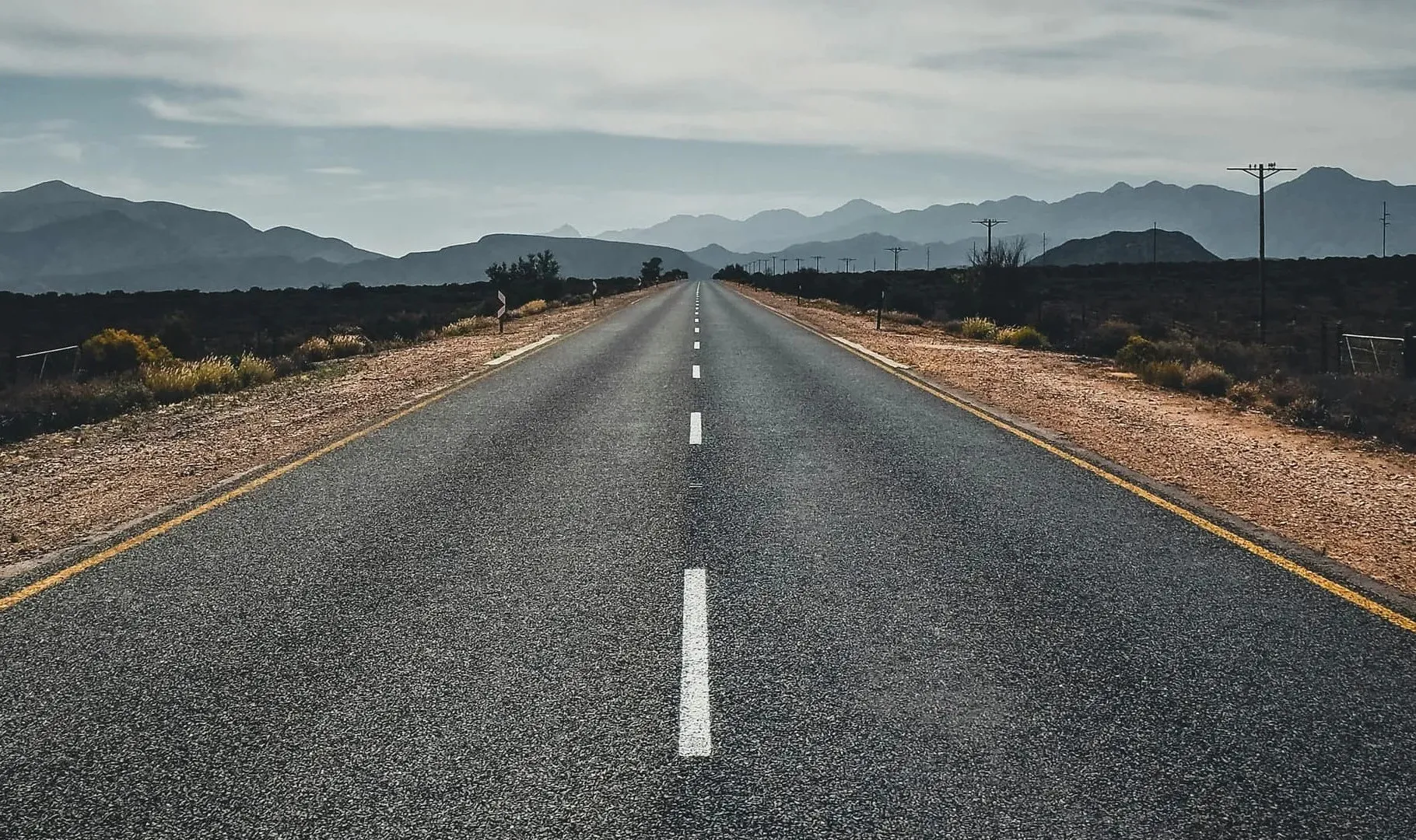 A long asphalt road disappearing into the horizon towards mountains